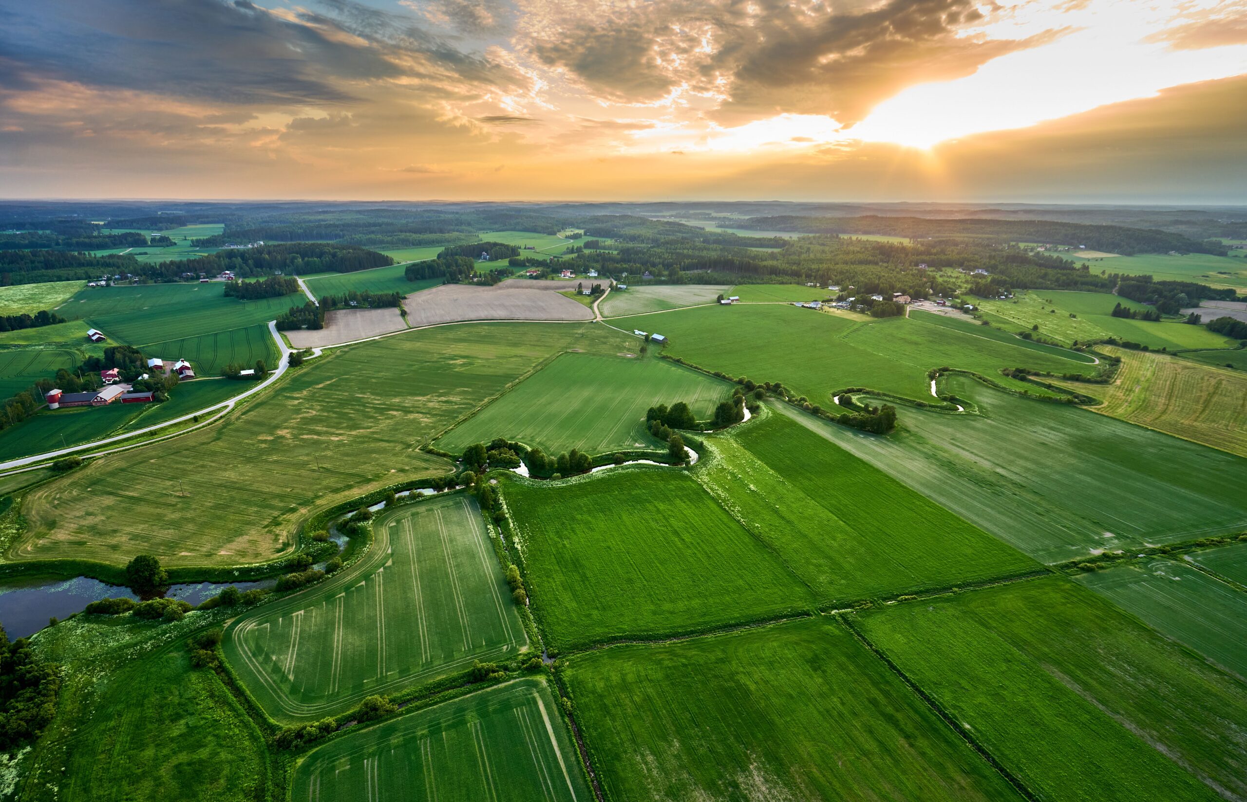 An aerial view of a rural landscape featuring a river snaking through green fields and farmland